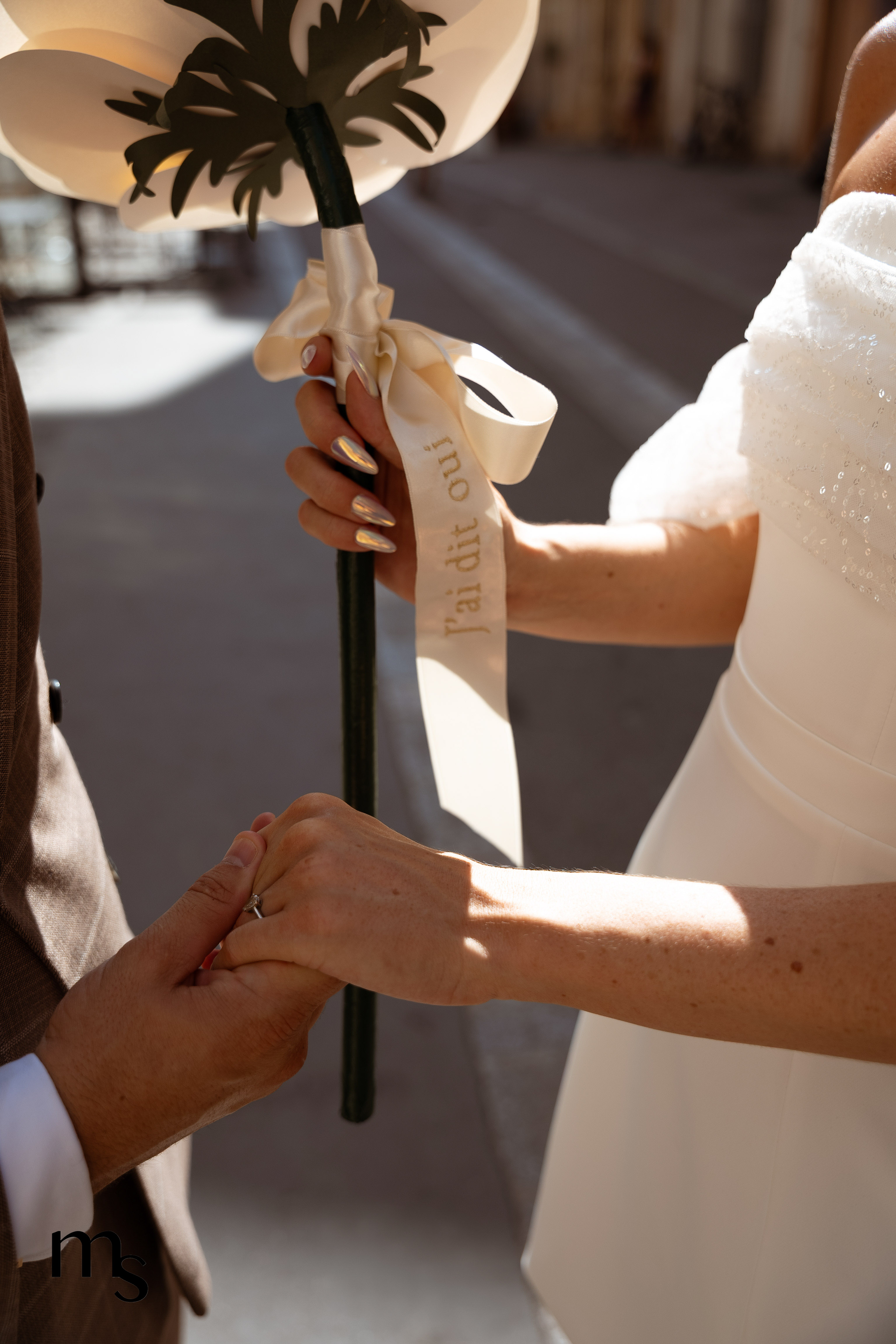 Jeunes mariés se donnant la main, fleur en papier avec message "j'ai dit oui" et bague de fiançailles, à Aix-en-Provence